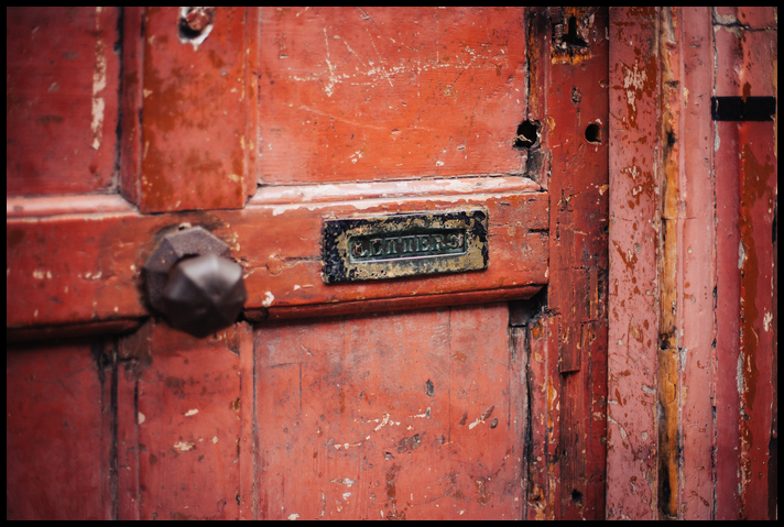 A letter slot on an old, banged up door.