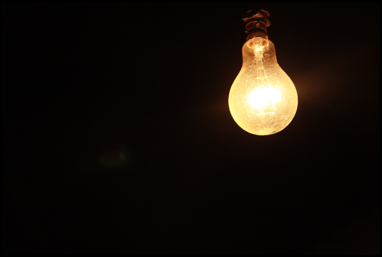Single bright, old-fashioned lightbulb against black background.